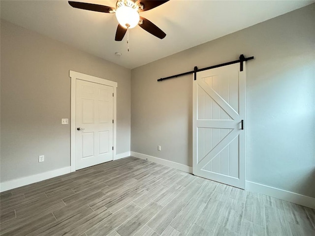 unfurnished bedroom featuring a barn door, hardwood / wood-style flooring, and ceiling fan