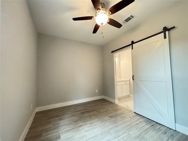 unfurnished bedroom featuring ensuite bathroom, a barn door, and ceiling fan