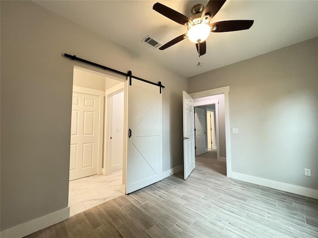 unfurnished bedroom featuring a barn door, light hardwood / wood-style floors, and ceiling fan