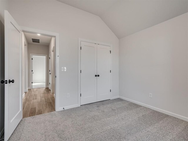 unfurnished bedroom featuring vaulted ceiling, light carpet, and a closet