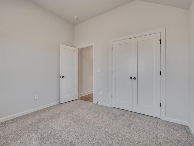 unfurnished bedroom featuring vaulted ceiling, light colored carpet, and a closet