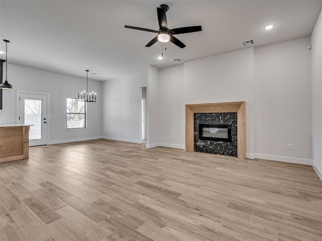 unfurnished living room featuring a fireplace, ceiling fan with notable chandelier, and light wood-type flooring