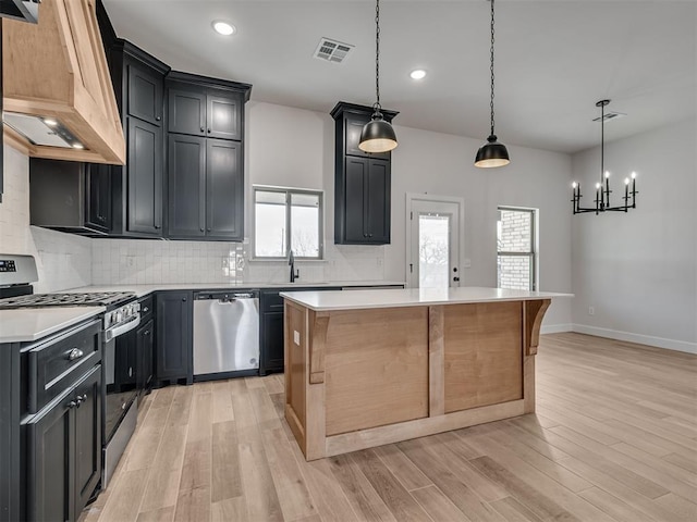 kitchen featuring a kitchen island, appliances with stainless steel finishes, decorative light fixtures, decorative backsplash, and custom range hood