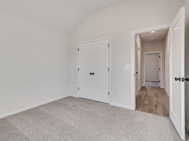 unfurnished bedroom featuring vaulted ceiling, light colored carpet, and a closet