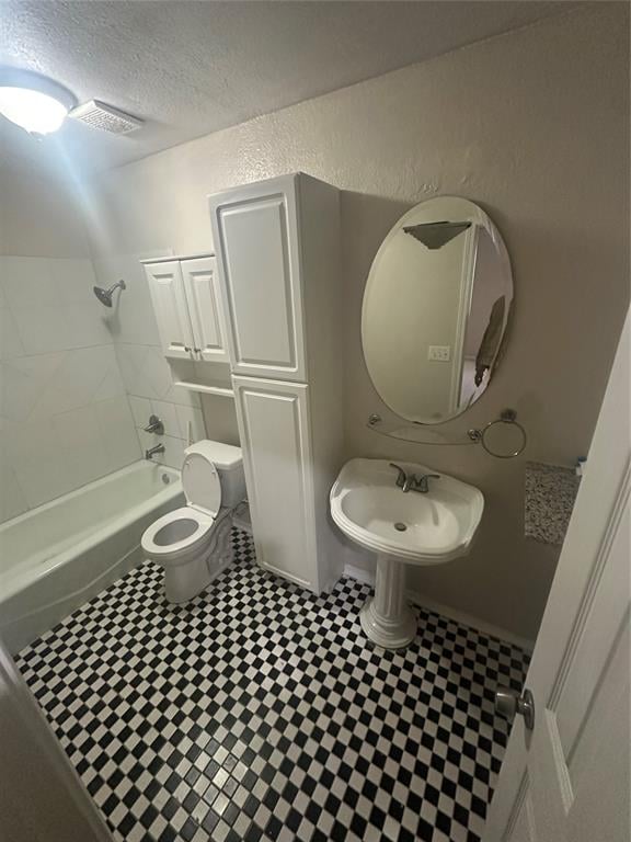 full bathroom featuring a textured ceiling, toilet, tiled shower / bath, and sink