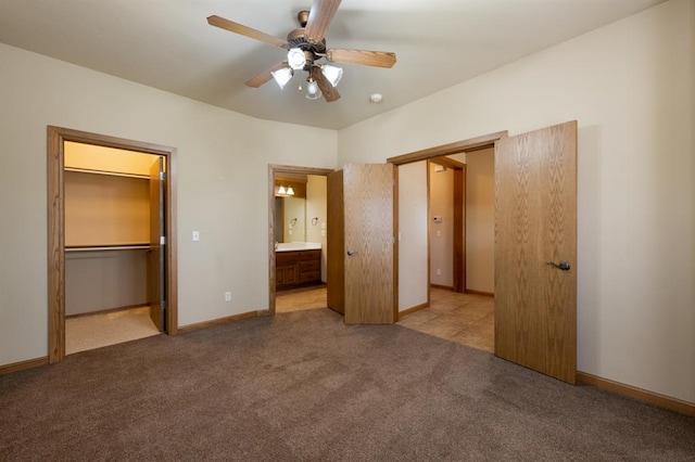 unfurnished bedroom featuring light carpet, a walk in closet, ensuite bath, ceiling fan, and a closet