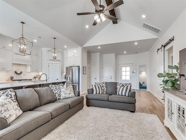 1718 Zayden Ln, Norman, OK 73072 - living room featuring high vaulted ceiling, ceiling fan with notable chandelier, a barn door, light wood-type flooring, and beam ceiling