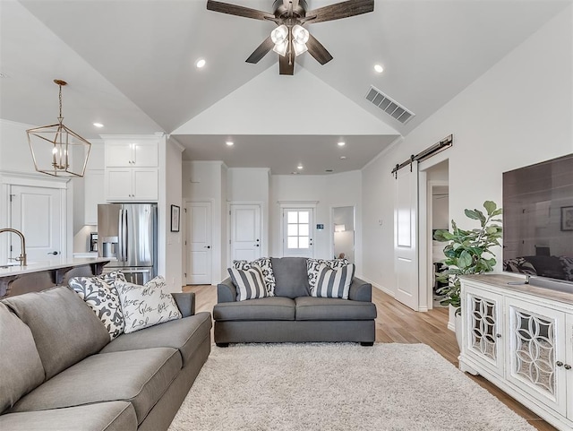 1718 Zayden Ln, Norman, OK 73072 - living room with high vaulted ceiling, ceiling fan with notable chandelier, sink, a barn door, and light hardwood / wood-style floors