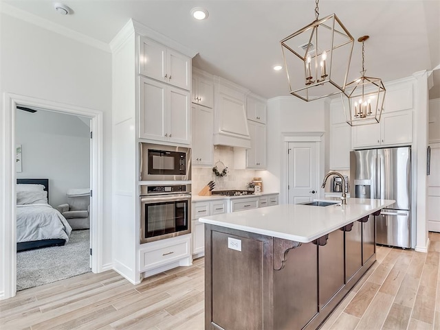 1718 Zayden Ln, Norman, OK 73072 - kitchen featuring appliances with stainless steel finishes, a kitchen island with sink, sink, light hardwood / wood-style flooring, and white cabinetry