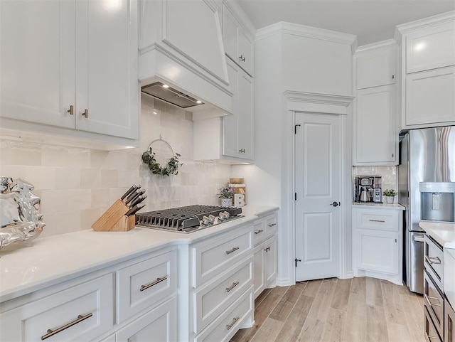 1718 Zayden Ln, Norman, OK 73072 - kitchen featuring backsplash, premium range hood, stainless steel appliances, light hardwood / wood-style floors, and white cabinetry