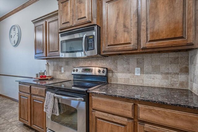 kitchen featuring backsplash, ornamental molding, dark stone counters, and appliances with stainless steel finishes