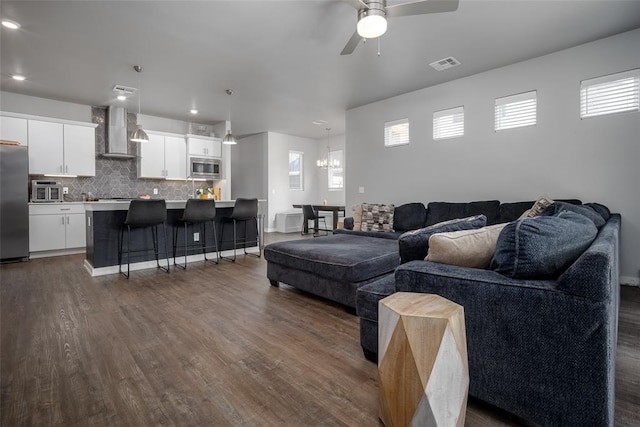 living room with ceiling fan with notable chandelier, a wealth of natural light, and dark wood-type flooring