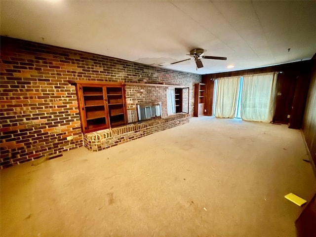 unfurnished living room with ceiling fan, brick wall, a fireplace, and carpet floors