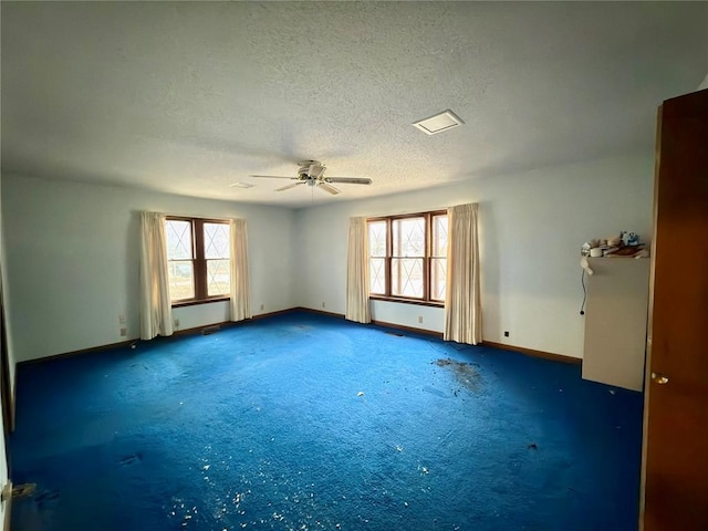 unfurnished room with dark colored carpet, a wealth of natural light, ceiling fan, and a textured ceiling