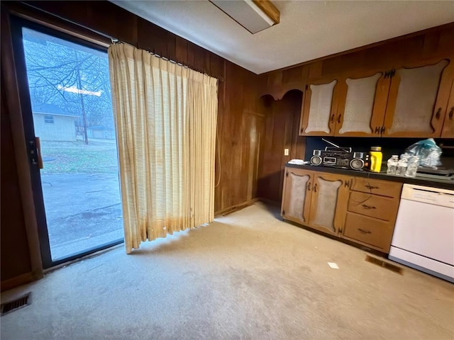 kitchen featuring dishwasher, light colored carpet, and wood walls