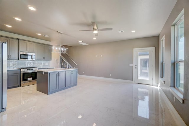 kitchen featuring appliances with stainless steel finishes, backsplash, decorative light fixtures, gray cabinets, and a kitchen island