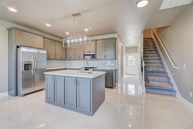 kitchen featuring pendant lighting, gray cabinetry, decorative backsplash, an island with sink, and appliances with stainless steel finishes