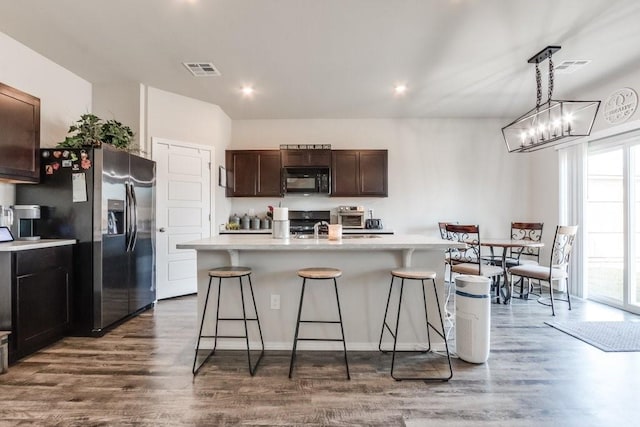 kitchen featuring a kitchen breakfast bar, dark brown cabinets, a kitchen island with sink, black appliances, and dark hardwood / wood-style floors