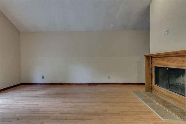 unfurnished living room featuring a tile fireplace, a textured ceiling, light hardwood / wood-style floors, and lofted ceiling