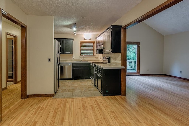 kitchen with sink, light hardwood / wood-style floors, a textured ceiling, vaulted ceiling, and appliances with stainless steel finishes