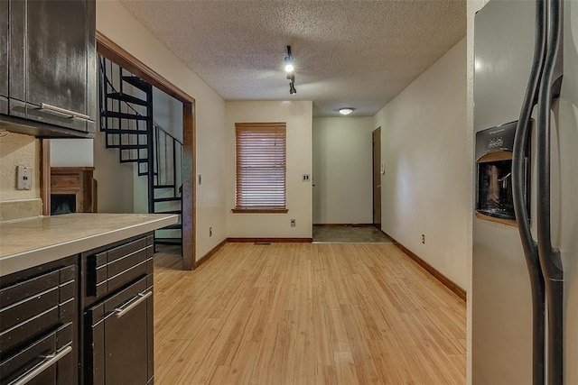 kitchen with a textured ceiling, dark brown cabinets, light hardwood / wood-style flooring, and stainless steel refrigerator with ice dispenser