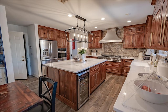 kitchen featuring wall chimney exhaust hood, beverage cooler, wood-type flooring, a kitchen island, and appliances with stainless steel finishes