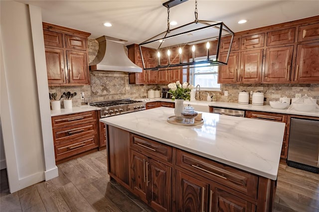 kitchen featuring a center island, premium range hood, dark hardwood / wood-style floors, decorative light fixtures, and light stone counters