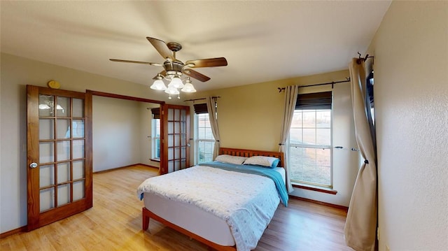 bedroom with french doors, light wood-type flooring, multiple windows, and ceiling fan