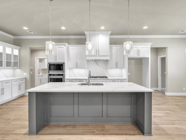 kitchen with a large island with sink, hanging light fixtures, white cabinets, and stainless steel appliances