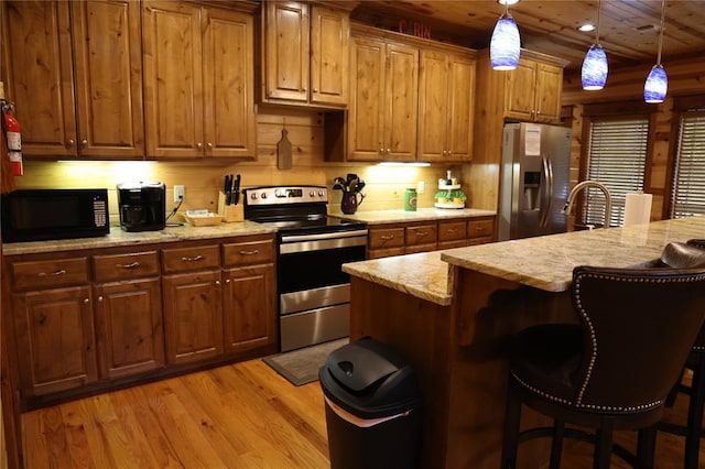 kitchen with hanging light fixtures, stainless steel appliances, light hardwood / wood-style floors, a breakfast bar area, and a kitchen island with sink