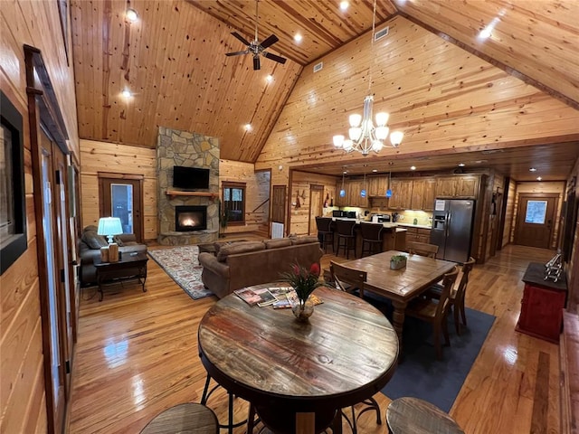 dining space with wooden ceiling, a stone fireplace, light hardwood / wood-style flooring, high vaulted ceiling, and ceiling fan with notable chandelier