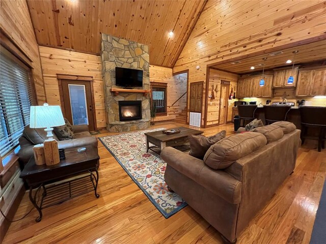 living room with wooden ceiling, light hardwood / wood-style flooring, high vaulted ceiling, and a stone fireplace