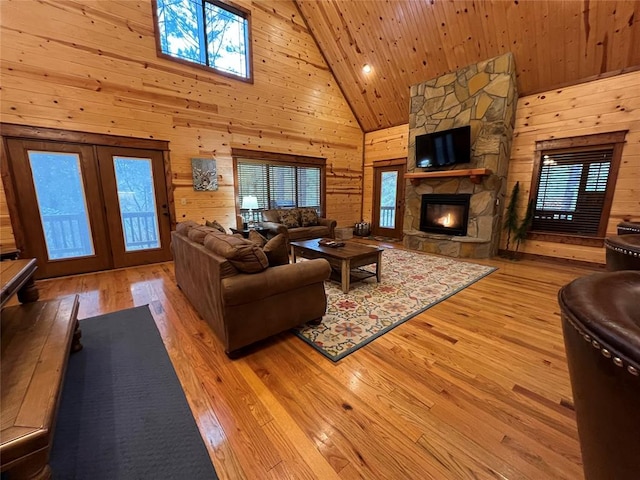 living room with a stone fireplace, a wealth of natural light, high vaulted ceiling, and light hardwood / wood-style floors