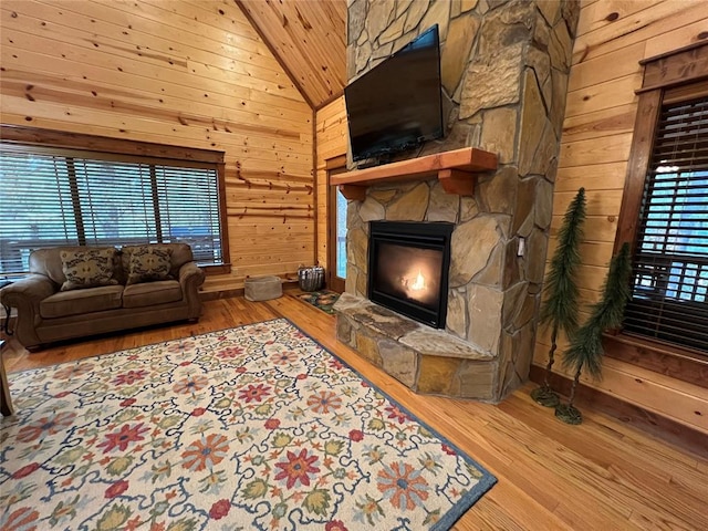 living room with hardwood / wood-style flooring, a stone fireplace, and wood walls