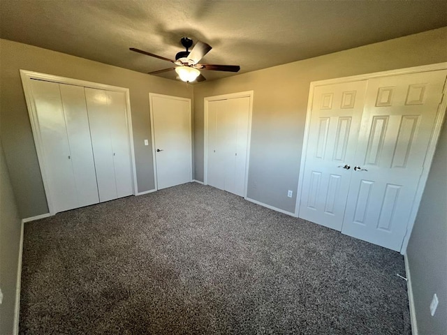 unfurnished bedroom with two closets, dark carpet, and ceiling fan