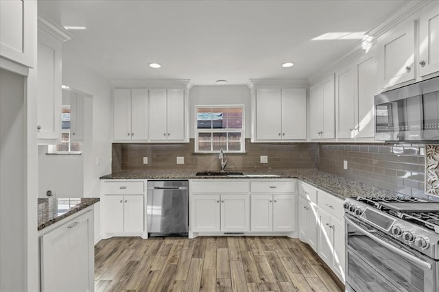 kitchen with white cabinetry, sink, stainless steel appliances, dark stone counters, and light wood-type flooring