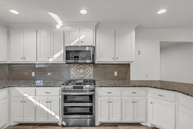 kitchen featuring white cabinets, appliances with stainless steel finishes, and dark stone counters