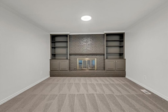 unfurnished living room featuring built in shelves, light colored carpet, a brick fireplace, and crown molding