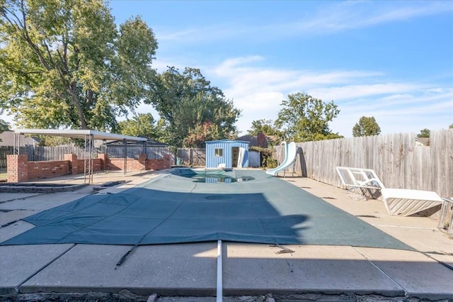 view of swimming pool featuring a patio area, a water slide, and a storage unit