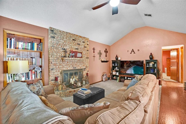 living room featuring lofted ceiling, hardwood / wood-style flooring, ceiling fan, a fireplace, and a textured ceiling