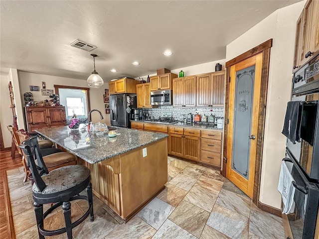 kitchen with a kitchen island with sink, visible vents, hanging light fixtures, appliances with stainless steel finishes, and tasteful backsplash