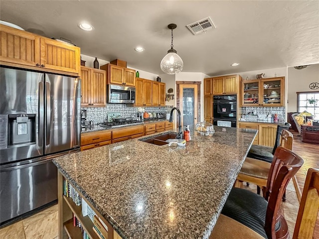 kitchen featuring brown cabinets, stainless steel appliances, a large island with sink, pendant lighting, and a sink