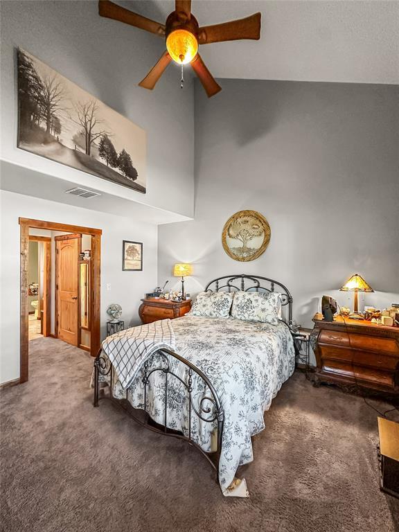 bedroom featuring a high ceiling, a ceiling fan, visible vents, baseboards, and dark carpet