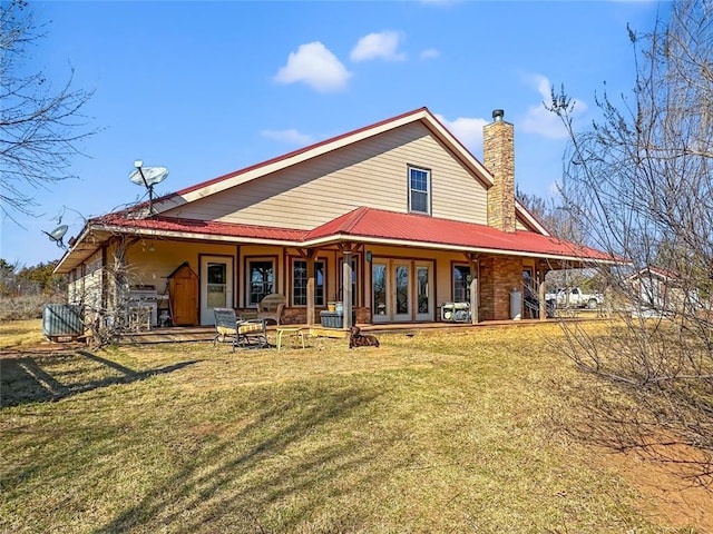 back of house featuring metal roof, a lawn, a chimney, and french doors