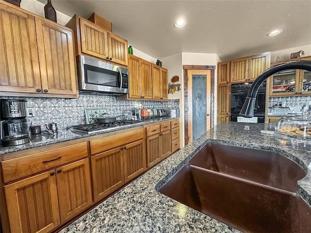 kitchen with stainless steel appliances, dark stone countertops, backsplash, and brown cabinets