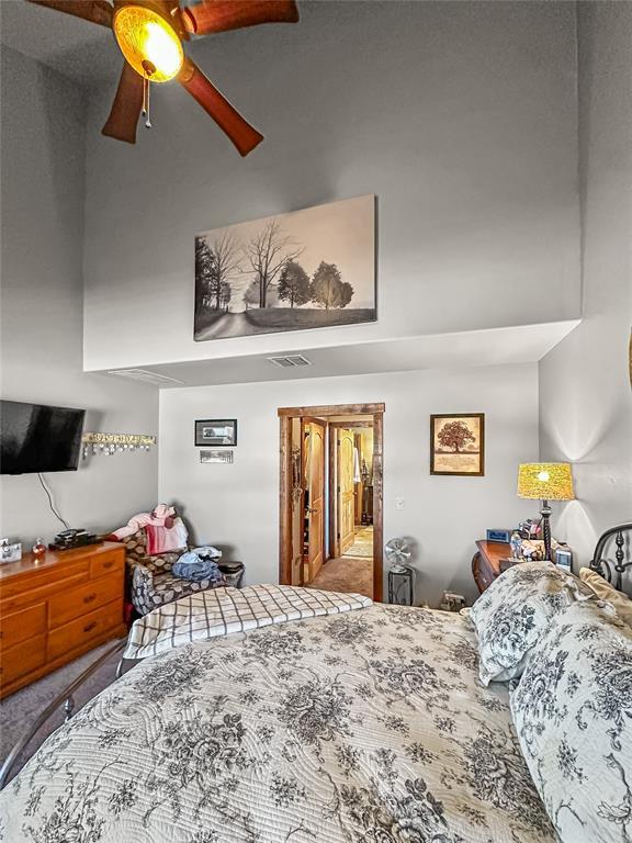 bedroom with carpet, a high ceiling, visible vents, and a ceiling fan