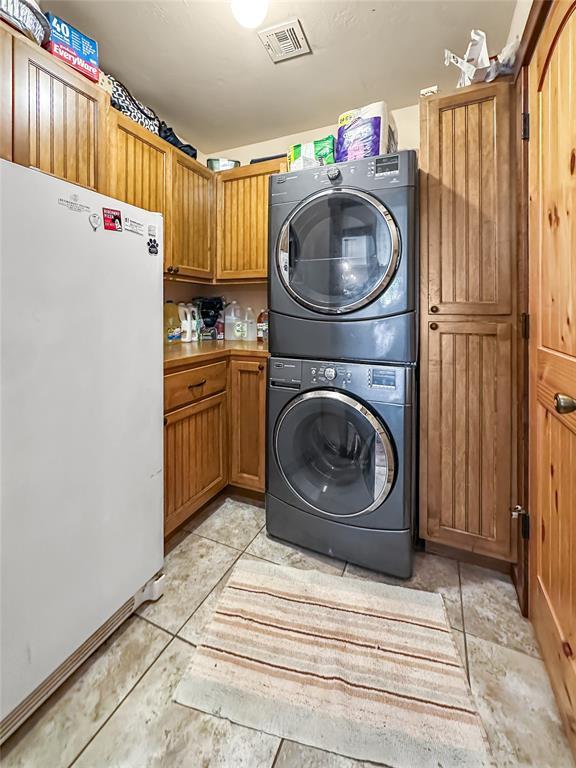 washroom featuring stacked washer and dryer, cabinet space, visible vents, and light tile patterned floors