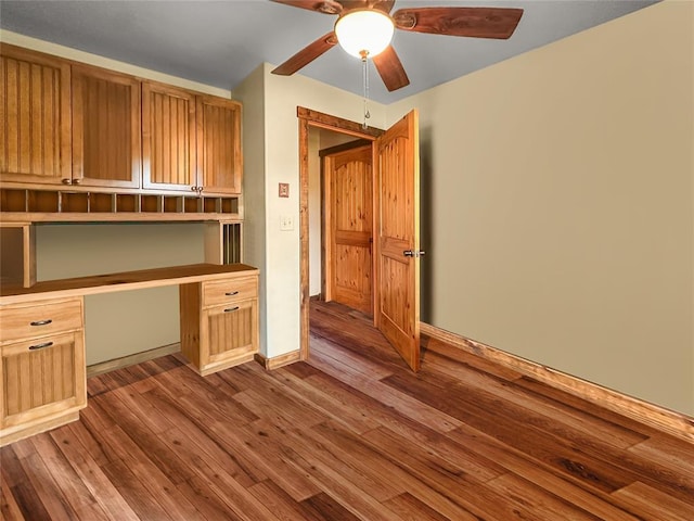 unfurnished office featuring ceiling fan, built in desk, light wood-style flooring, and baseboards