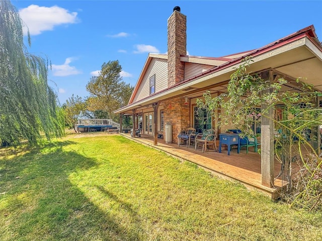 rear view of house featuring a lawn, a chimney, and a wooden deck