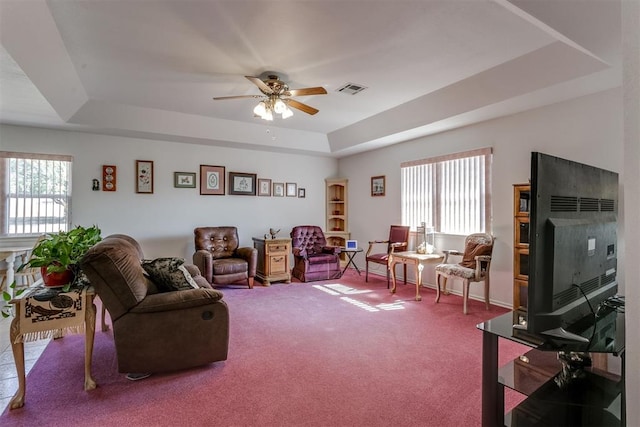 carpeted living room featuring a raised ceiling, ceiling fan, and a healthy amount of sunlight